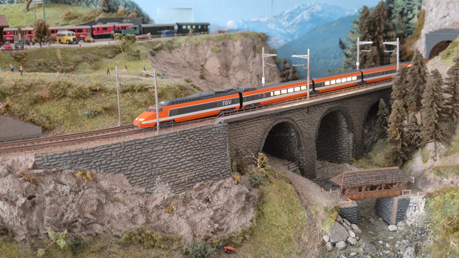Ein Modell eines TGV-Zugs fährt über eine vierspännige Steinbrücke in einer detaillierten Landschaften mit Bäumen und Bergen im Hintergrund.