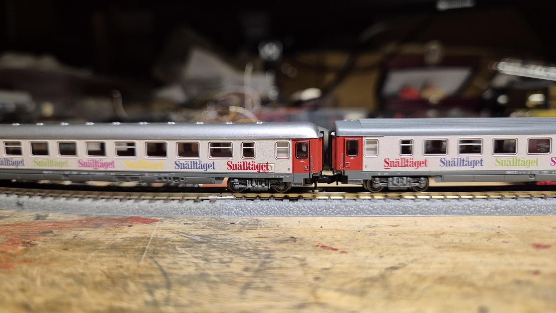 Zwei Modelleisenbahn-Wagen mit der Aufschrift Snälltåget auf den Seiten, auf einem Gleis platziert.
